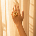 Load image into Gallery viewer, Unbound Flick Wearable Ring Vibrator in 24K Gold, held in hand for size comparison